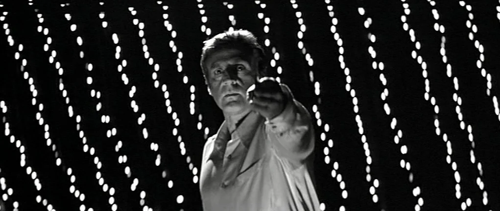 Girl on the Bridge (1999) movie still: medium — A man stands centered in a dark space against a backdrop of vertical light strands. The man extends…