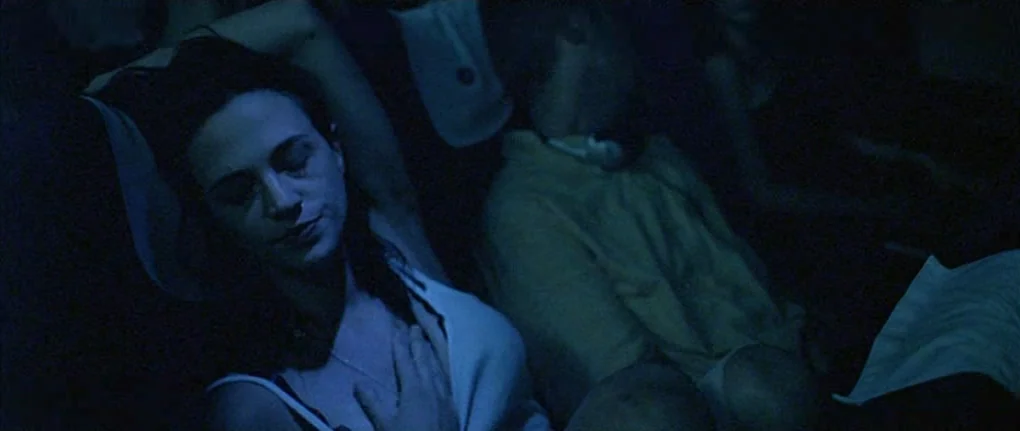 Boarding Gate (2007) movie still: medium — The interior of an airplane cabin is dark, illuminated primarily by artificial screen light. A woman…