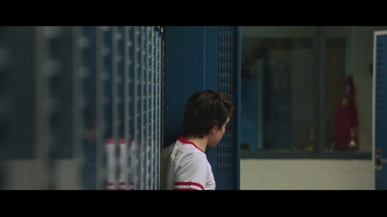 Collective: Unconscious (2016) movie still: medium — A row of blue metal lockers lines a bright school hallway wall. A young male student stands in…