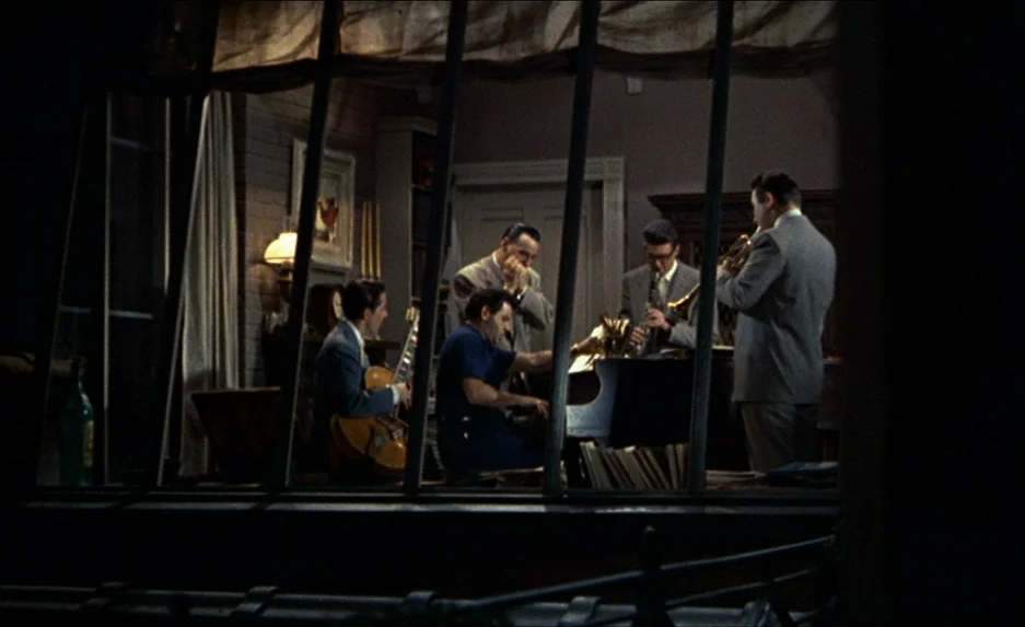 Rear Window (1954) movie still: wide — A jazz band practices in a room viewed through a window frame with bars. The musicians play piano, clarinet,…