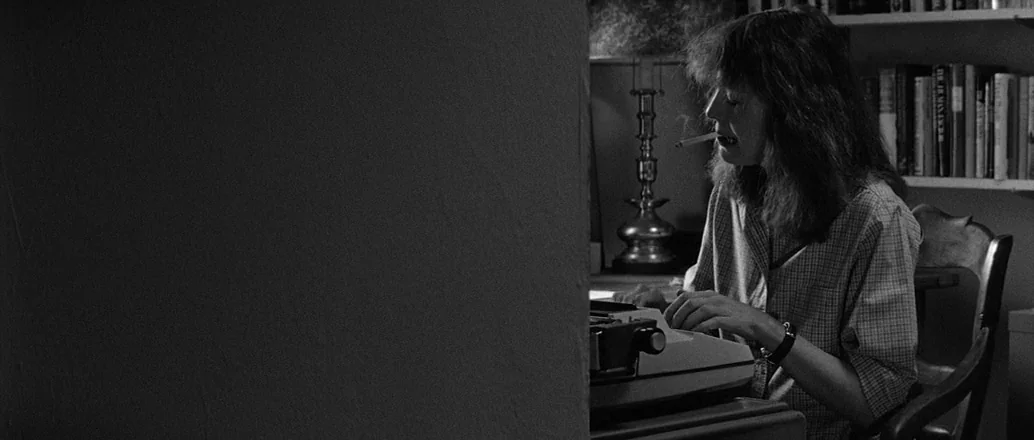 Manhattan (1979) movie still: medium — A dimly lit home study features a wall of books and a desk lamp. A woman sits at a desk using a typewriter…