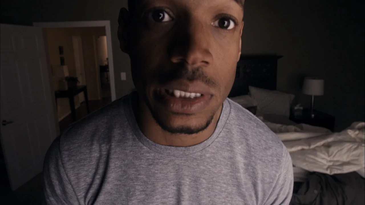 A Haunted House (2013) movie still: closeup — A dimly lit bedroom features an unmade bed and an open doorway in the background. A man stands close…