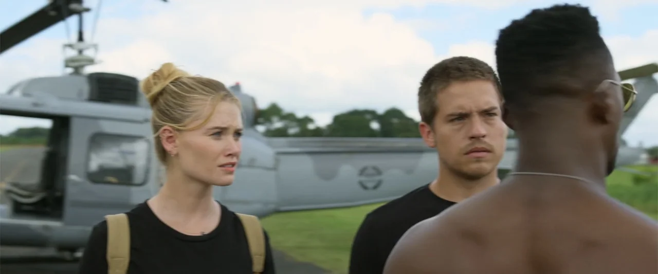 Beautiful Wedding (2024) movie still: medium — Three individuals stand outdoors near a gray helicopter parked on a grassy landing area. They look…