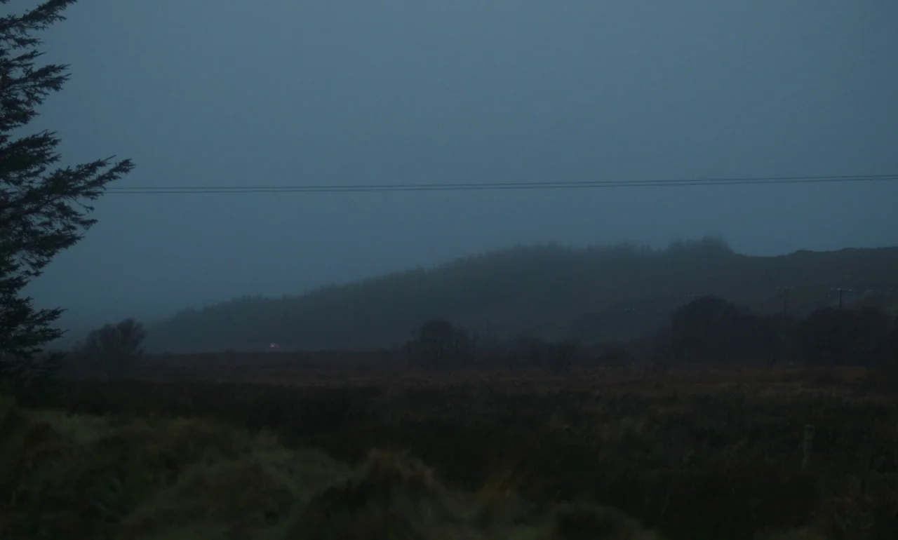 It Is In Us All (2022) movie still: wide — A dark, misty moorland extends under an overcast sky during the late twilight hours. A singular…