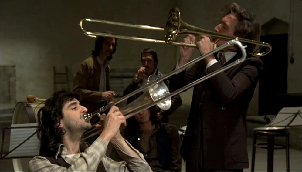 Orchestra Rehearsal (1978) movie still: medium — A sparsely furnished, dimly lit rehearsal room with bare concrete walls and equipment. Two men in…