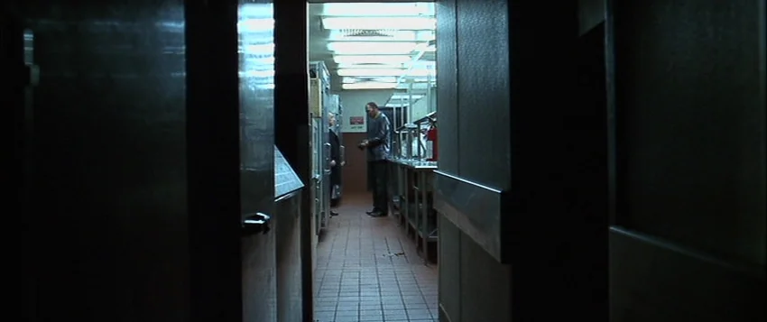 Hard Eight (1996) movie still: wide — A dark, narrow service corridor leads into a brightly lit commercial stainless steel kitchen. Two men stand in…