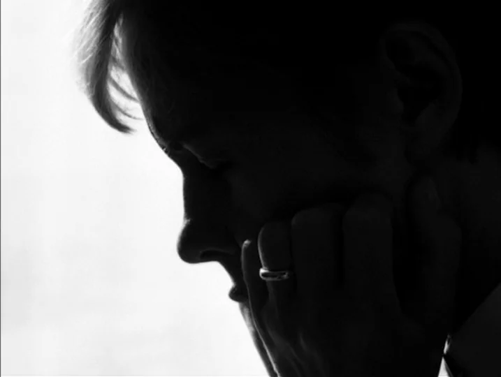 Persona (1966) movie still: closeup — A close-up view of a person inside a brightly lit space. The subject rests their chin upon their hand with…