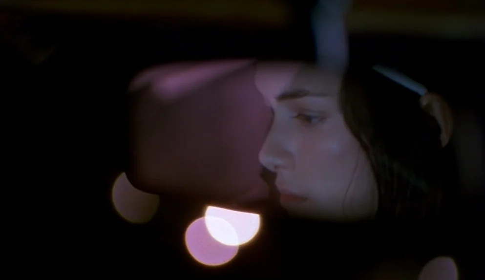Night on Earth (1991) movie still: closeup — A close view of a person inside a dark vehicle at night. Bokeh light reflections are visible on the…