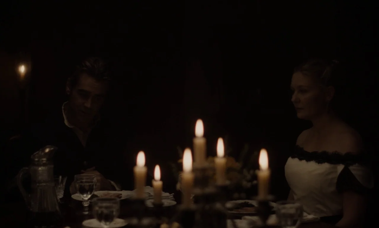 The Beguiled (2017) (2017) movie still: medium — A dimly lit room with a wooden table set for dinner. A man and a woman sit facing one another by…