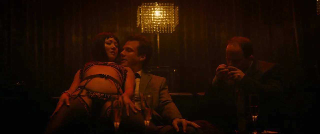 Hustlers (2019) movie still: medium — A dimly lit club booth features dark curtains and a central hanging crystal chandelier. A woman wearing…