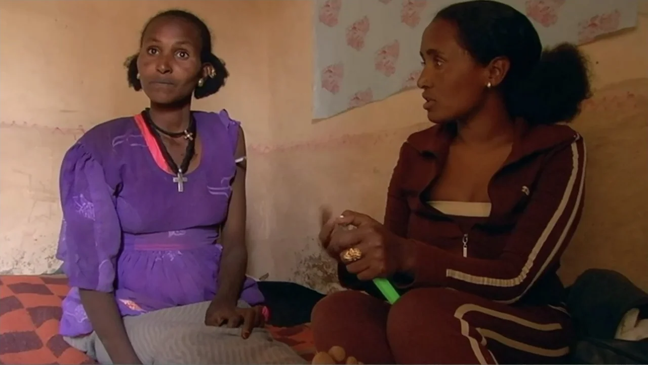 Sister (2014) movie still: medium — A small interior bedroom features plain walls and simple furniture. Two women sit on a bed while talking to each…