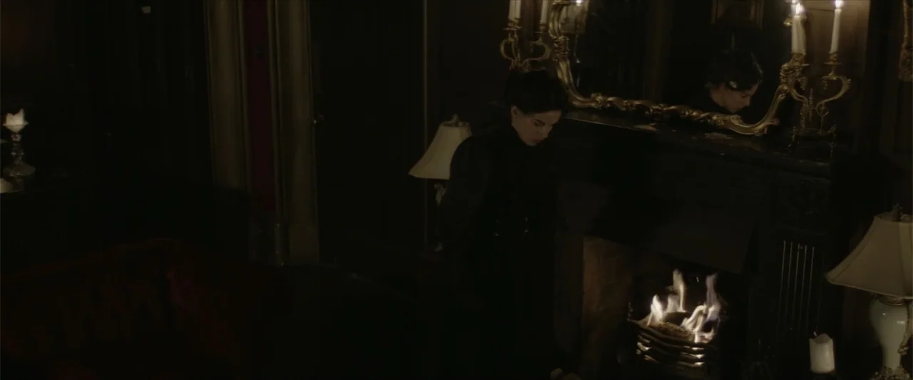 Cinderella's Curse (2024) movie still: medium — A dimly lit Victorian parlor features a dark fireplace with a large ornate mirror. A young woman in…