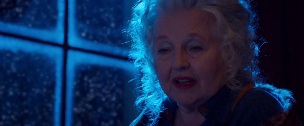 Peter Von Kant (2022) movie still: closeup — An interior space is illuminated by a cold blue light source from a window. An elderly woman with curly…