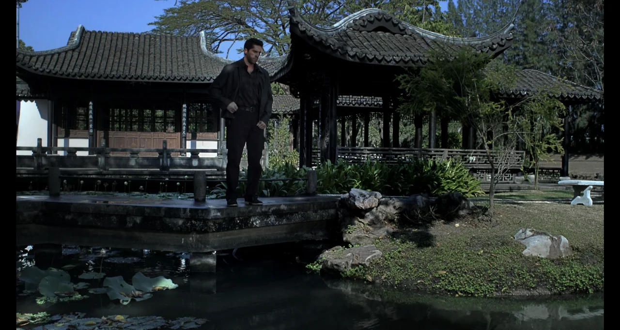 Ninja: Shadow of a Tear (2013) movie still: fullbody — A traditional stone bridge crosses a pond in a quiet, well-maintained Chinese garden. A man…