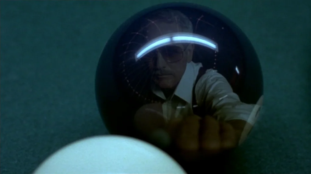 The Colour of Money (1986) movie still: closeup — A pool table with green felt features a dark ball and a white ball. A man's face is clearly…