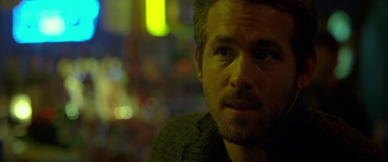 Mississippi Grind (2015) movie still: closeup — A dimly lit bar environment with blurred neon signage visible in the bokeh background. A man with…