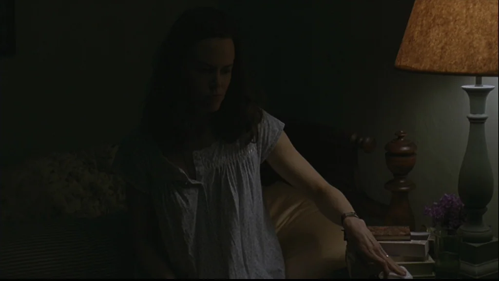 Margot At The Wedding (2007) movie still: medium — A dimly lit room with muted earth tones and low shadow detail. A woman in a nightgown reaches for…