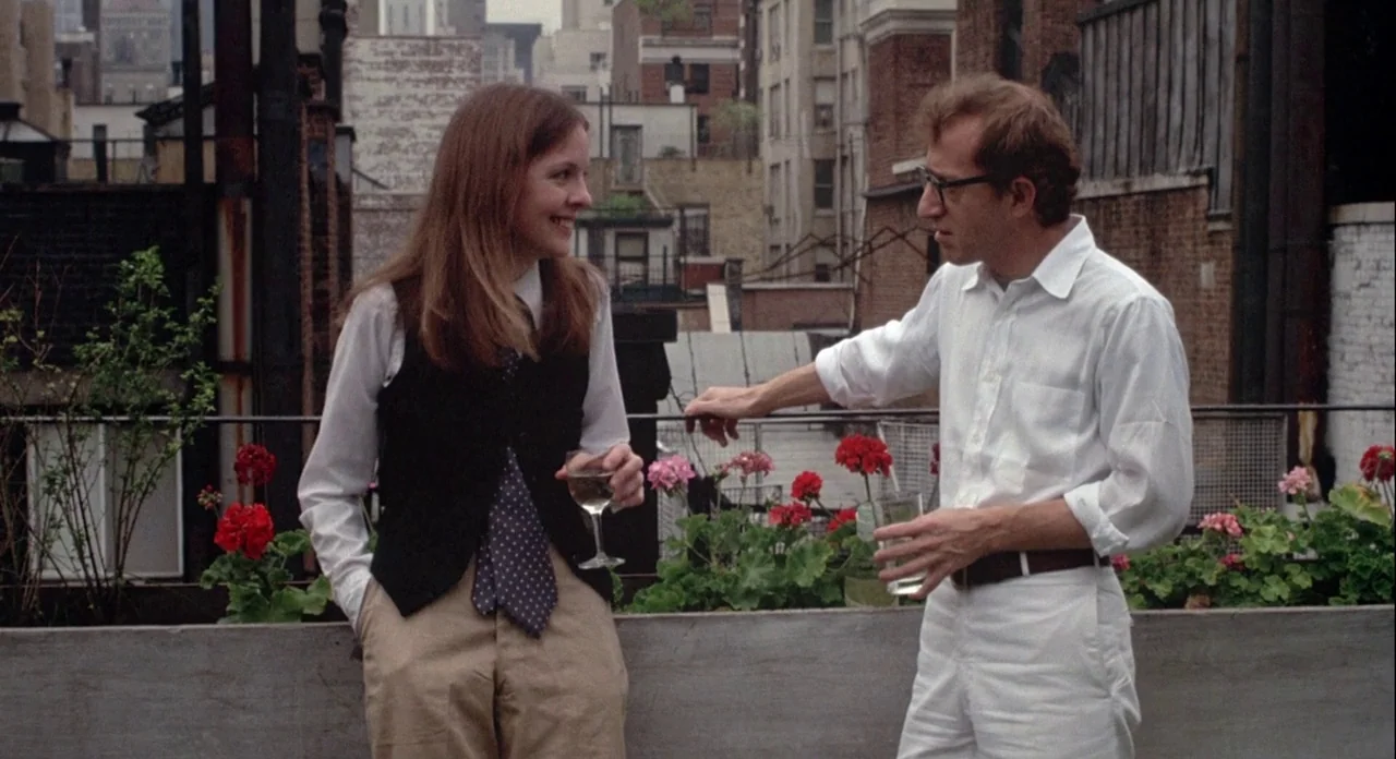 Annie Hall (1977) movie still: medium — A city rooftop features concrete planters filled with red flowers and lush green foliage. A man and a woman…