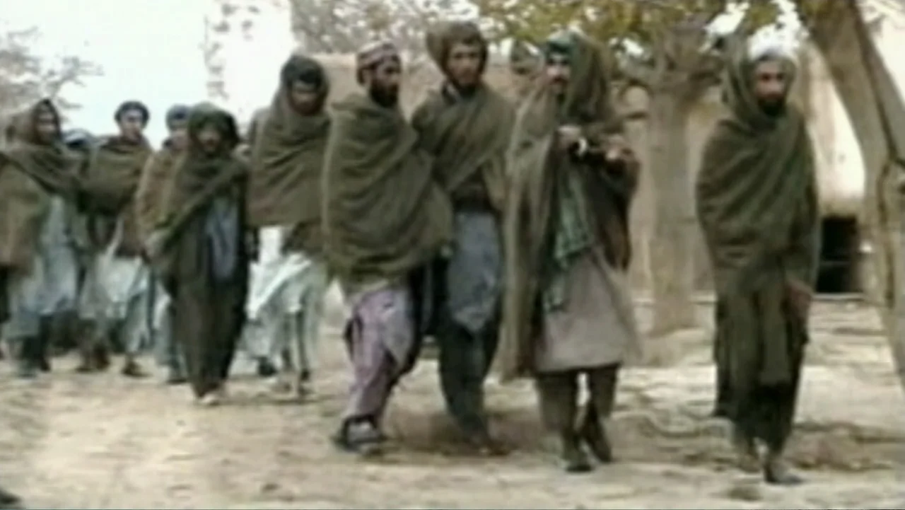 Ghosts of Abu Ghraib (2007) movie still: fullbody — A group of men walk along a dusty path lined with bare trees. The men wear traditional robes and…