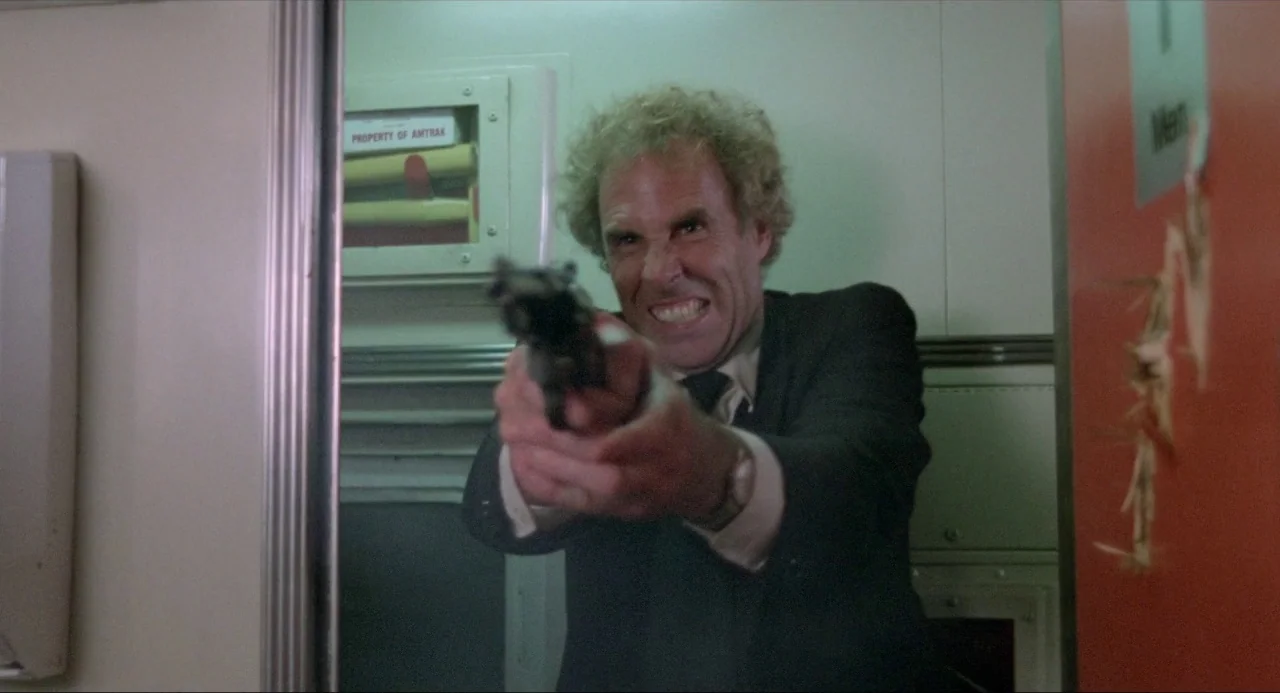 The Driver (1978) movie still: medium — A narrow train corridor features an Amtrak-labeled utility cabinet and a red door panel. A middle-aged man…
