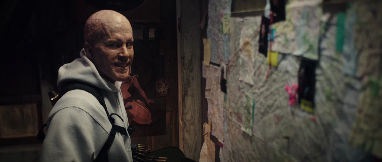 Deadpool (2016) movie still: medium — A dimly lit, cramped interior space features a wall covered in various notes and photos. A man with a scarred,…