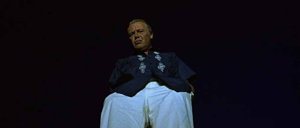 Sexy Beast (2000) movie still: medium — An elderly man is framed from a low angle against a dark night sky. The man stares down directly into the…