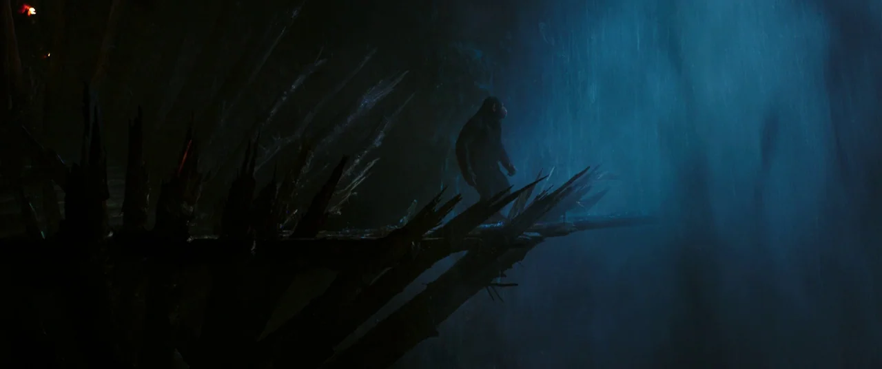 War for the Planet of the Apes (2017) movie still: wide — A chimpanzee walks across a dark, jagged wooden structure in front of a waterfall. The…