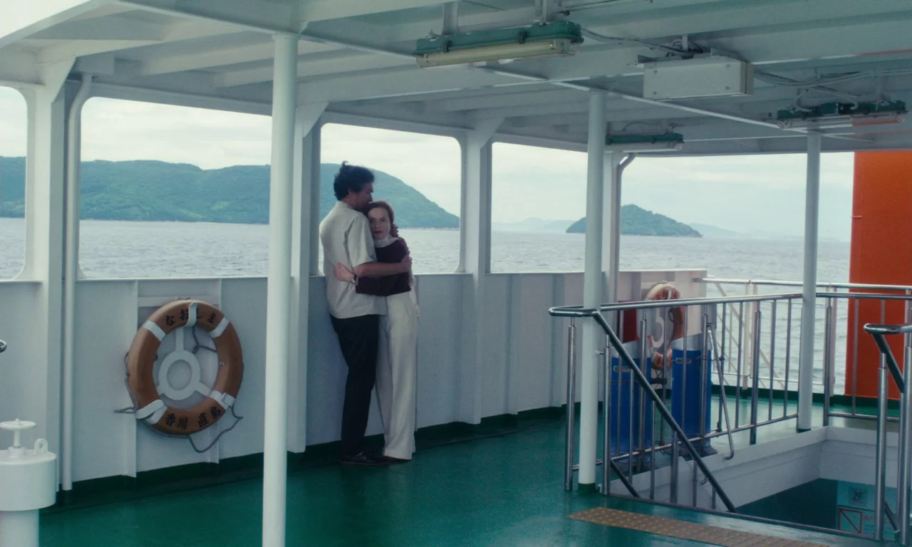 Sidonie in Japan (2023) movie still: fullbody — An open deck of a ferry with white railings and green flooring during daytime. A man and a woman…