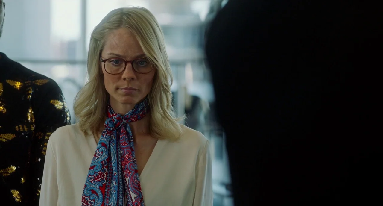 Rabid (2019) movie still: medium — A modern interior setting with a blurred background showing glass walls and bright light. A blonde woman with…
