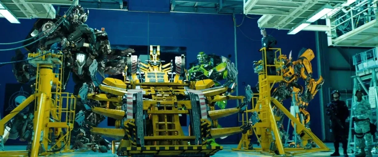 Transformers: Dark of the Moon (2011) movie still: wide — A high-ceilinged blue industrial hangar contains large yellow maintenance platforms and…