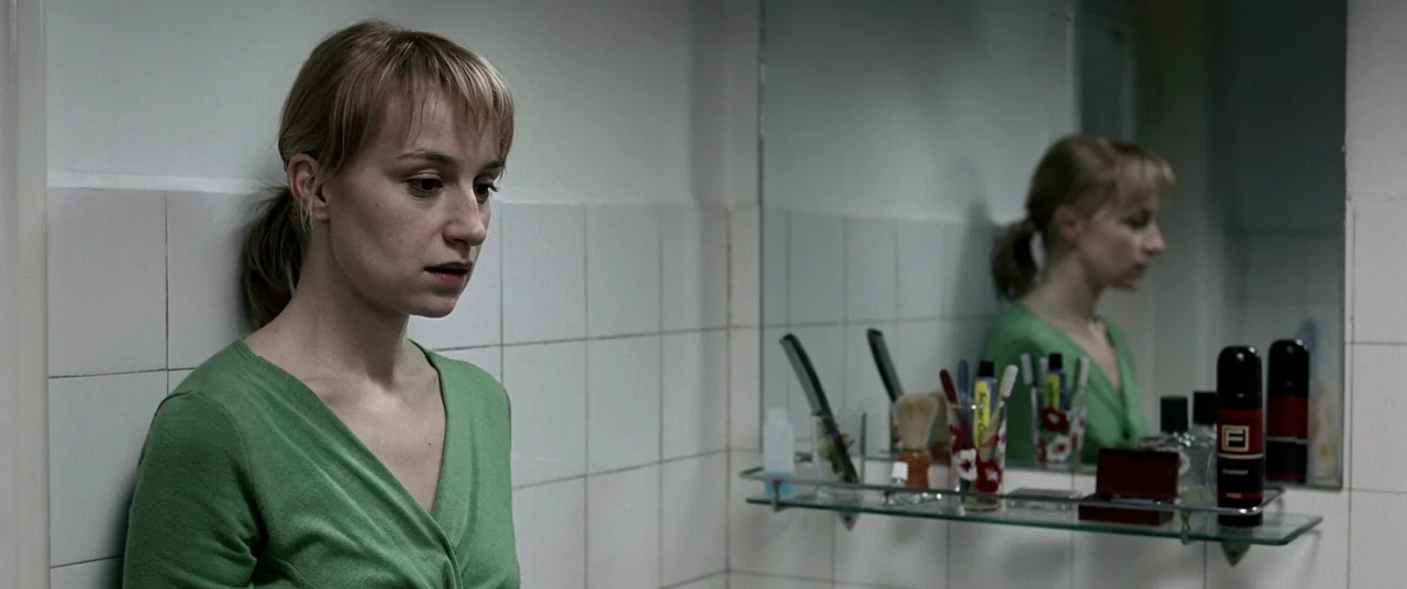 4 months, 3 Weeks and 2 Days (2007) movie still: medium — A small room features white square wall tiles and a glass vanity shelf. A young woman in a…
