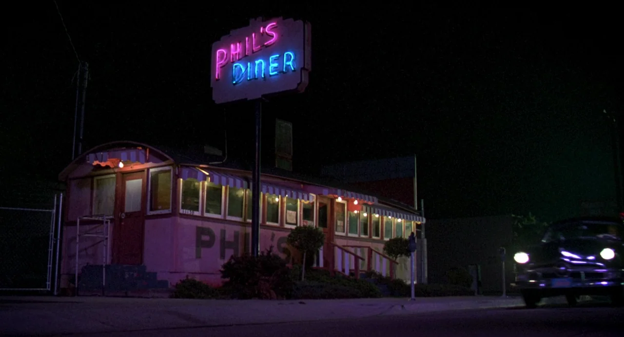 Night of the Creeps (1986) movie still: establishing — A roadside diner with painted walls sits against a dark night sky. A neon sign displays the…