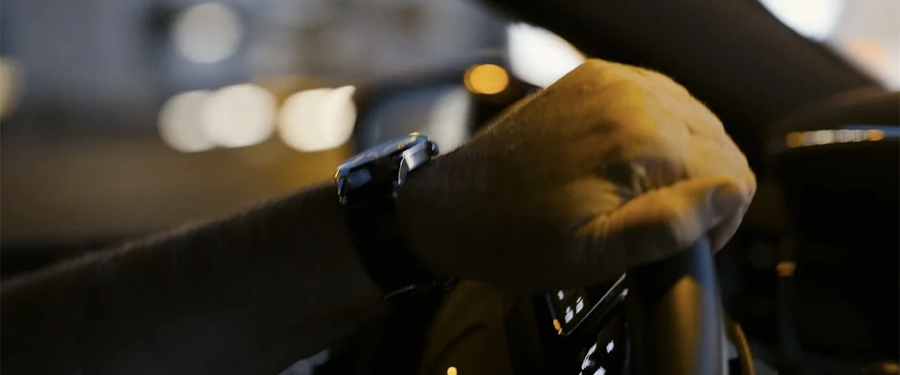 The Kleptocrats (2018) movie still: closeup — A dark car interior at night with blurred city lights visible through the window. A driver's arm is…