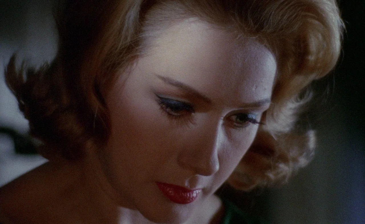 Blood And Black Lace (1964) movie still: closeup — A close view shows a woman in a dimly lit room with blonde hair. She looks downward with red…