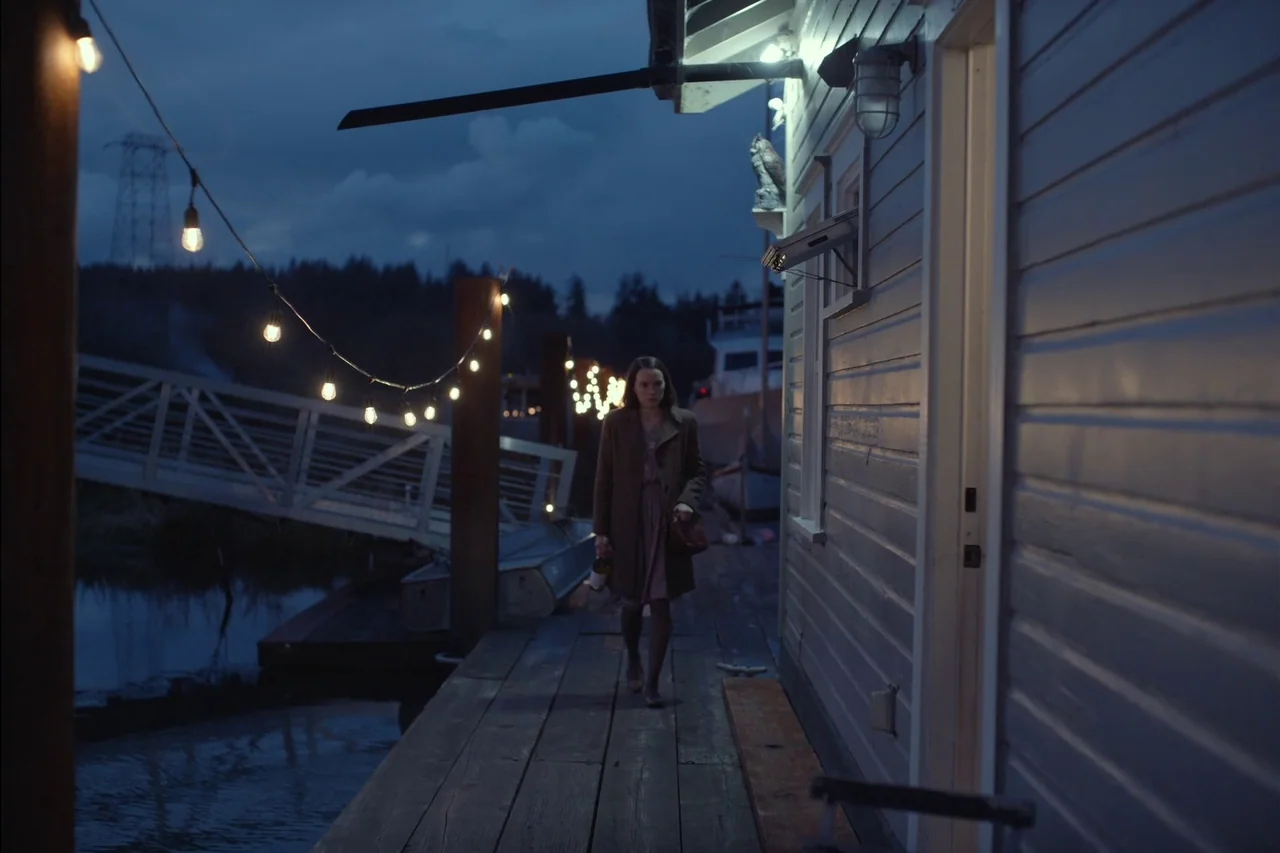 Sometimes I Think About Dying (2023) movie still: fullbody — A wooden pier at night sits beside a light-colored cabin-style structure on the water.…