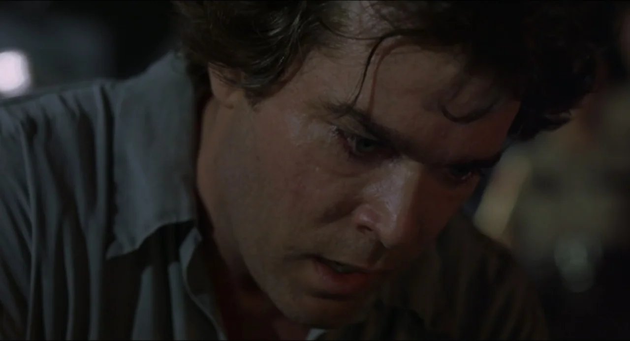 Cop Land (1997) movie still: closeup — A dimly lit room provides a dark background for the subject in close proximity. A man in a light gray shirt…
