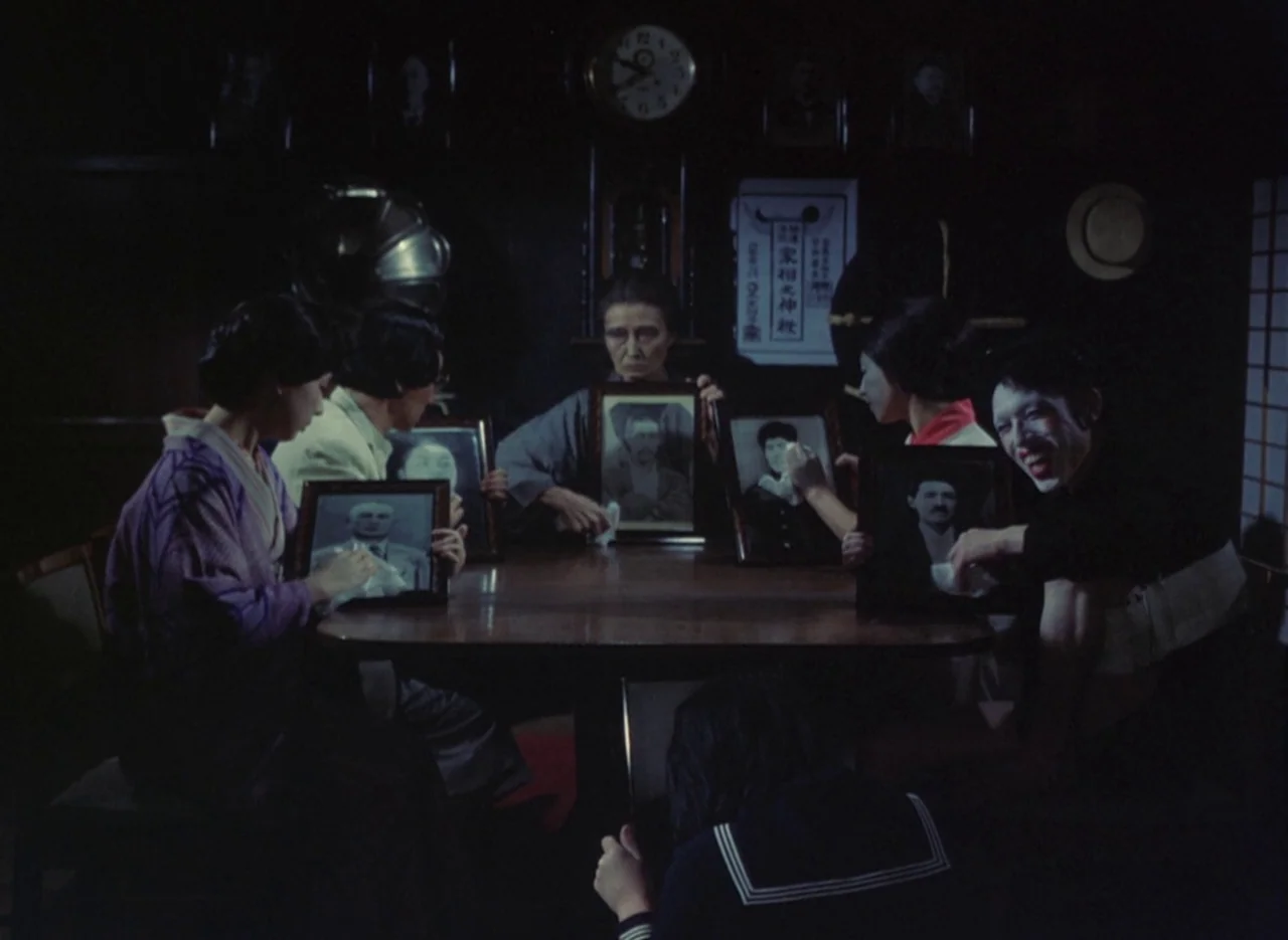 Pastoral To Die In The Country (1974) movie still: medium — A dark, wood-paneled room contains a central table surrounded by several figures. The…