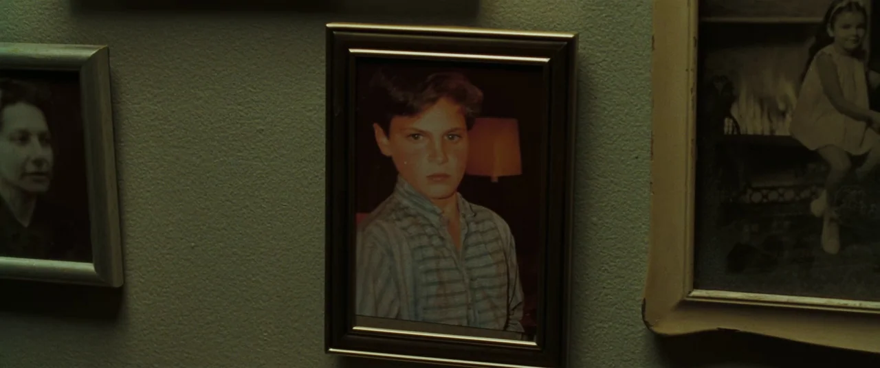 Two Lovers (2008) movie still: closeup — A framed portrait of a young boy hangs on a dim wall among other photos. The child looks forward in a…