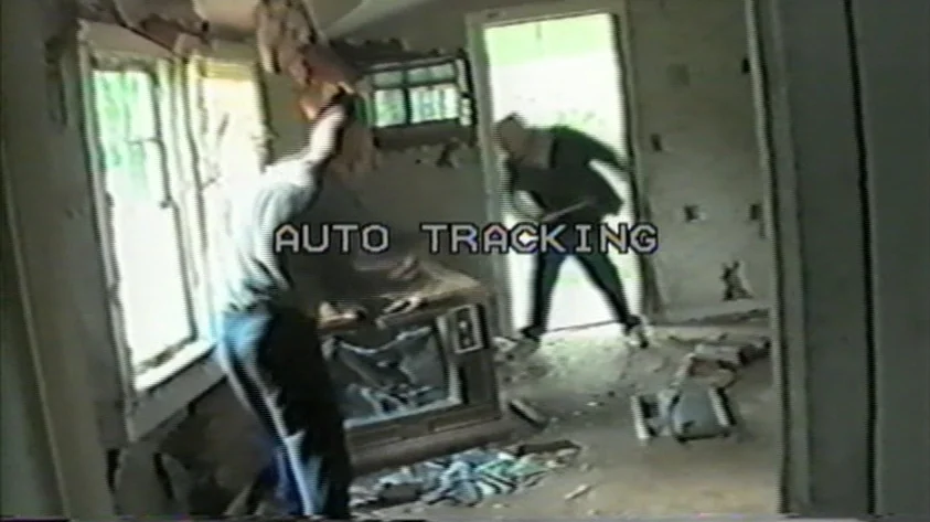 Trash Humpers (2009) movie still: fullbody — A neglected room features debris on the floor and a broken wooden console television. Two men navigate…