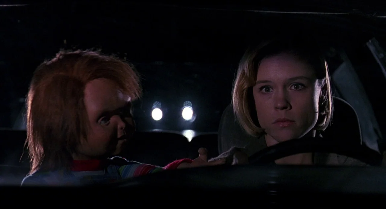 Child’s Play 2 (1990) movie still: medium — A dark car interior at night with headlights visible through the rear window. A woman drives while a…