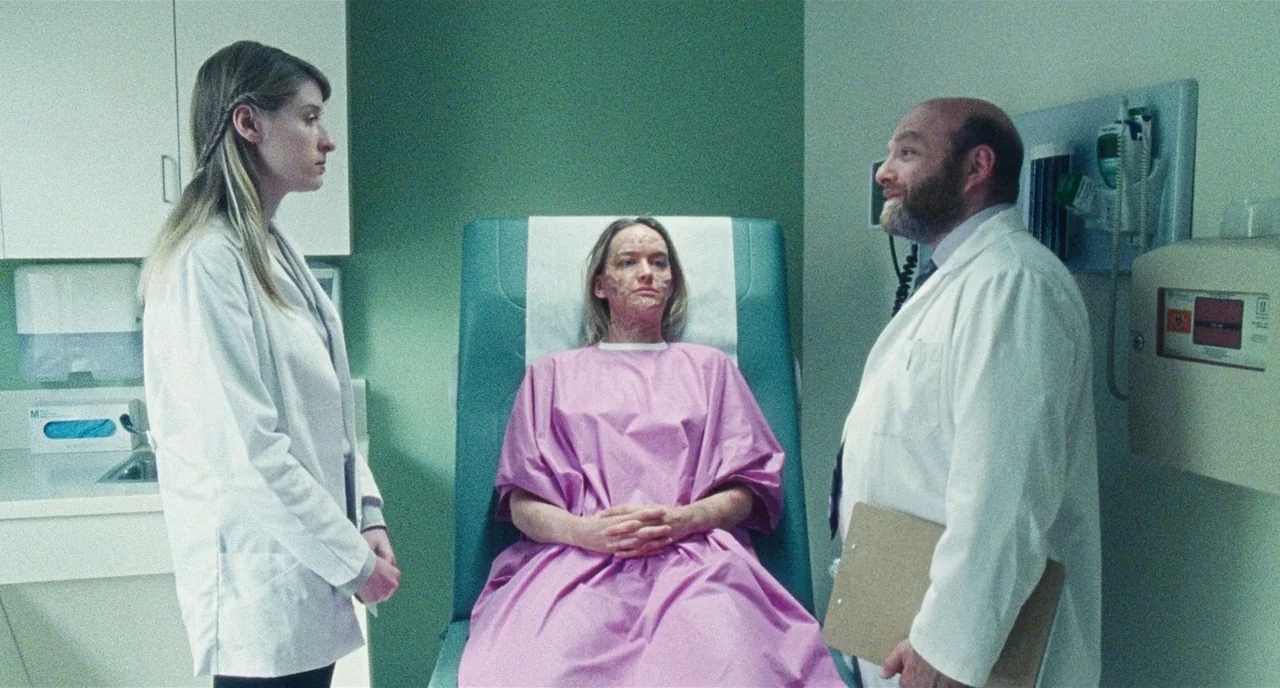 Chained For Life (2018) movie still: medium — A clinical examination room features green walls, white cabinets, and a diagnostic station. A patient…