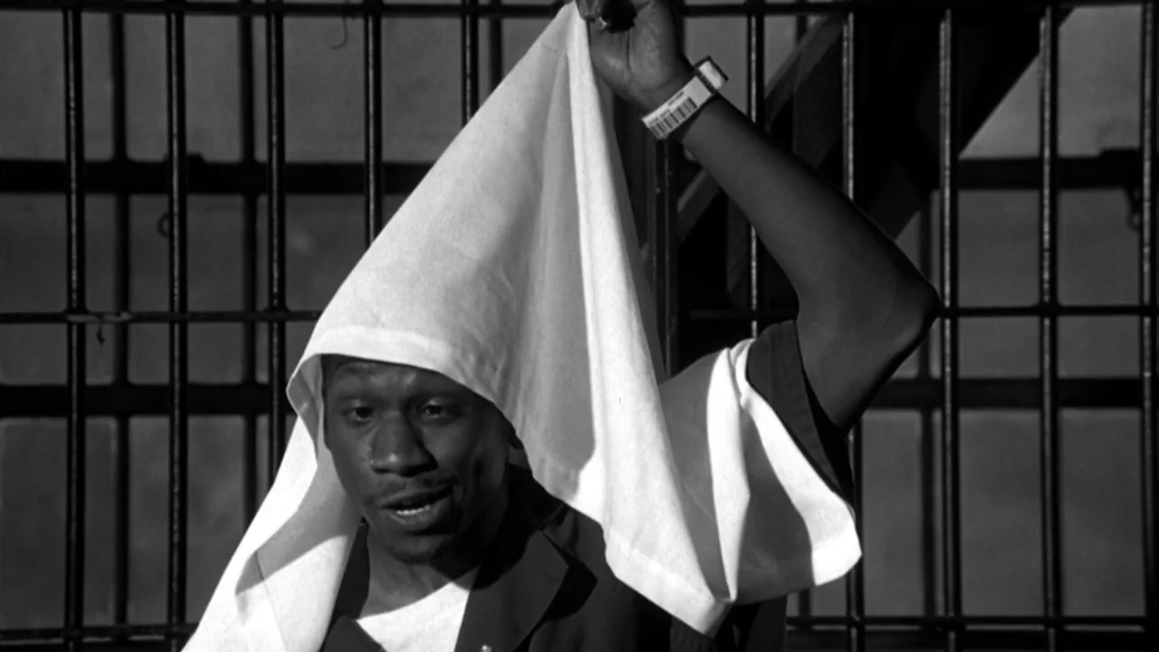 American History X movie still: medium — A dimly lit room defined by heavy vertical metal bars in the background. A man wears a dark jumpsuit while…