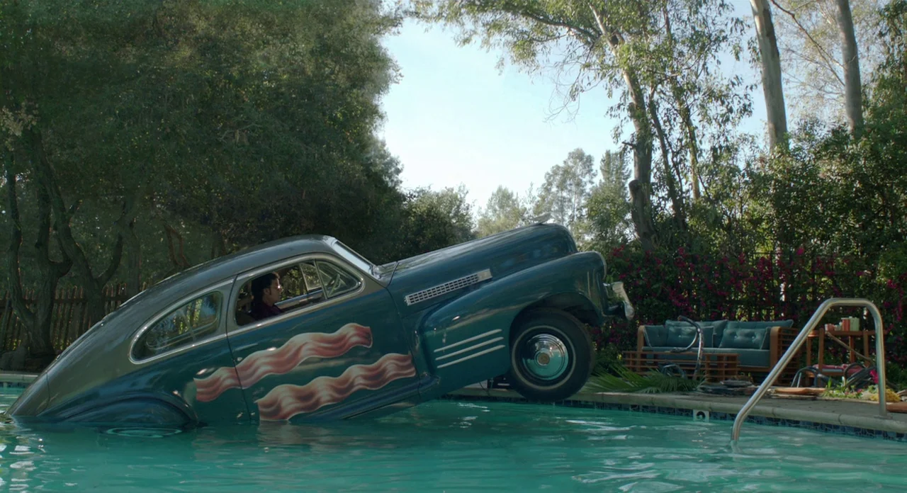 A Glimpse Inside The Mind Of Charles Swan III (2013) movie still: wide — A dark green vintage car with bacon graphics is submerged at an angle in…