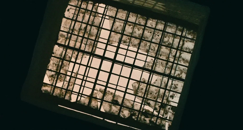 The Limits of Control (2009) movie still: closeup — A square, grid-patterned ceiling light fixture features cracked and damaged translucent panels.…