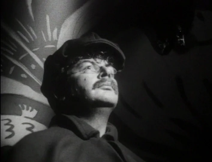 Archangel (1990) movie still: closeup — A man stands in a dimly lit room with painted patterns on the wall. He looks upward with a slight turn of…