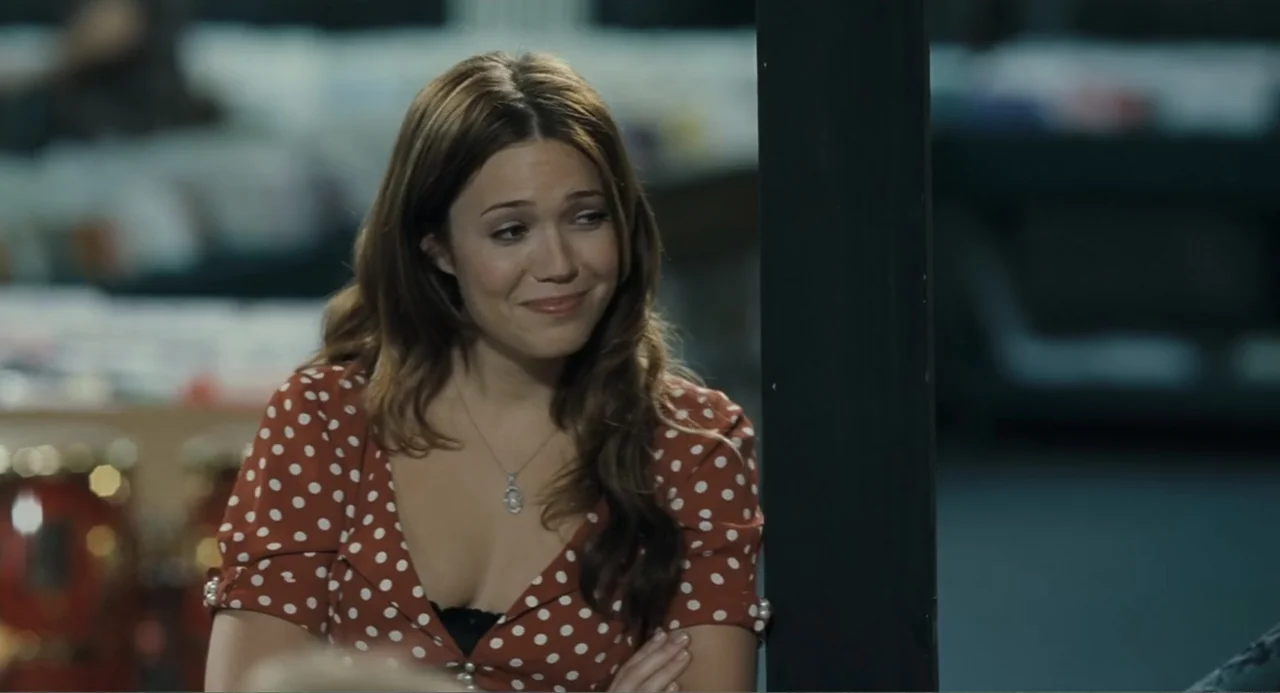 Because I Said So (2007) movie still: medium — A woman stands in a retail store interior with blurred shelves in the background. She wears a red…