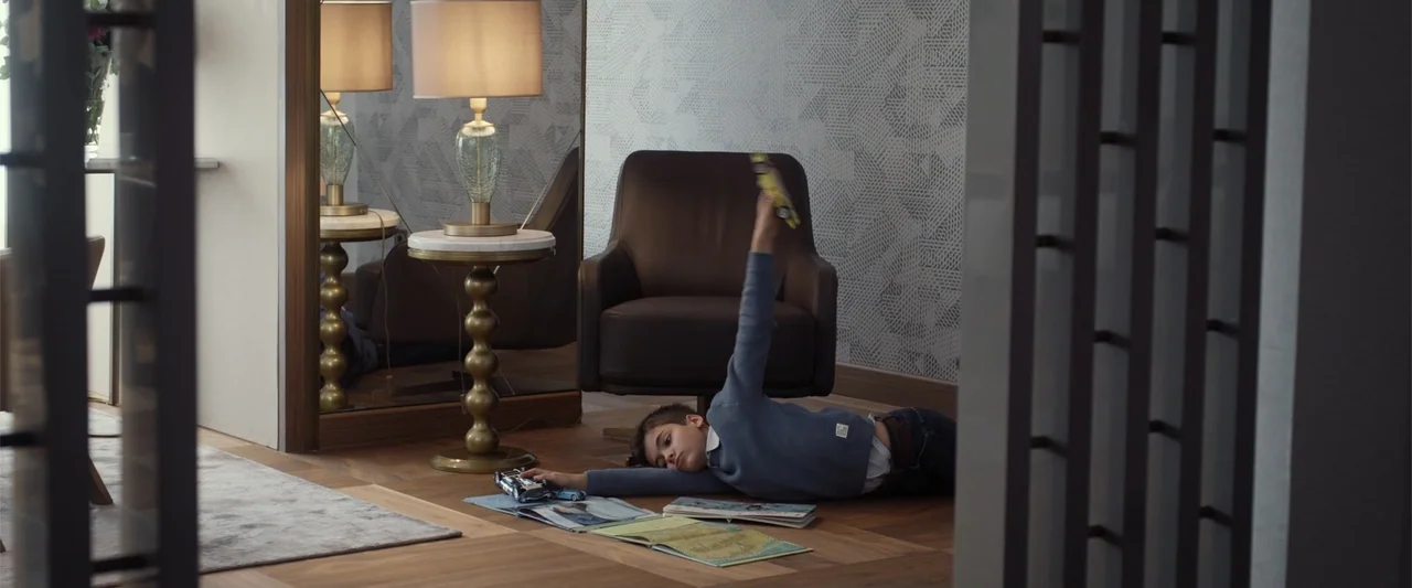 After Ever Happy (2022) movie still: medium — A modern interior space features patterned wallpaper, a brown armchair, and a tall mirror. A young boy…
