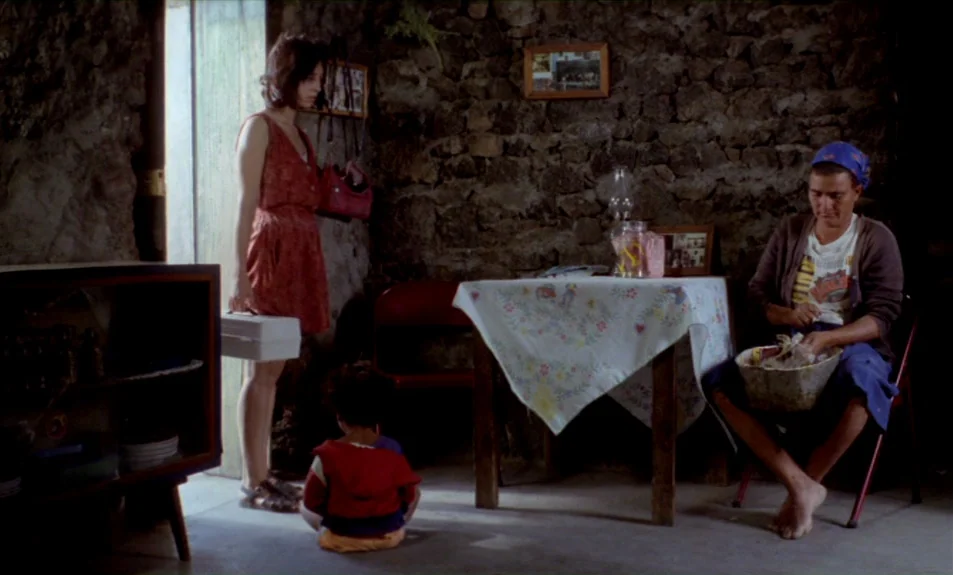 Casa De Lava (1994) movie still: fullbody — A rustic interior with exposed rough stone walls features a central wooden table. A woman holds a box by…