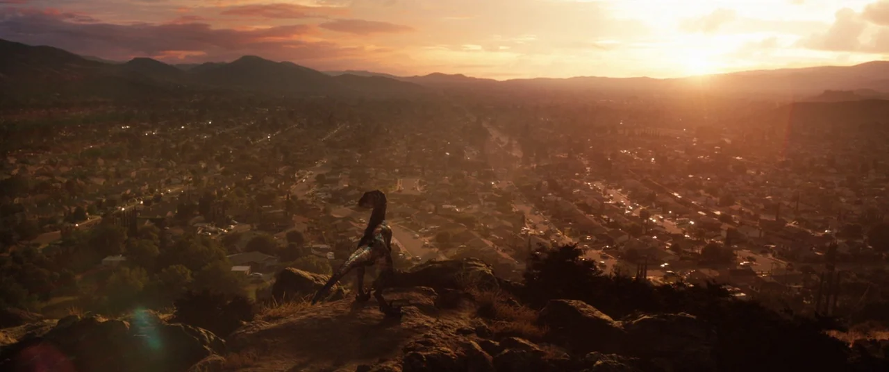 Jurassic World: Fallen Kingdom (2018) movie still: wide — A rocky hilltop overlooks a sprawling suburban valley during a clear, bright sunset. A…
