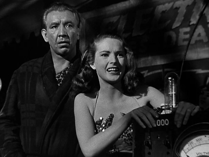 Nightmare Alley (1947) movie still: medium — A dimly lit room filled with mysterious electrical equipment and analog dials. A young woman and an…